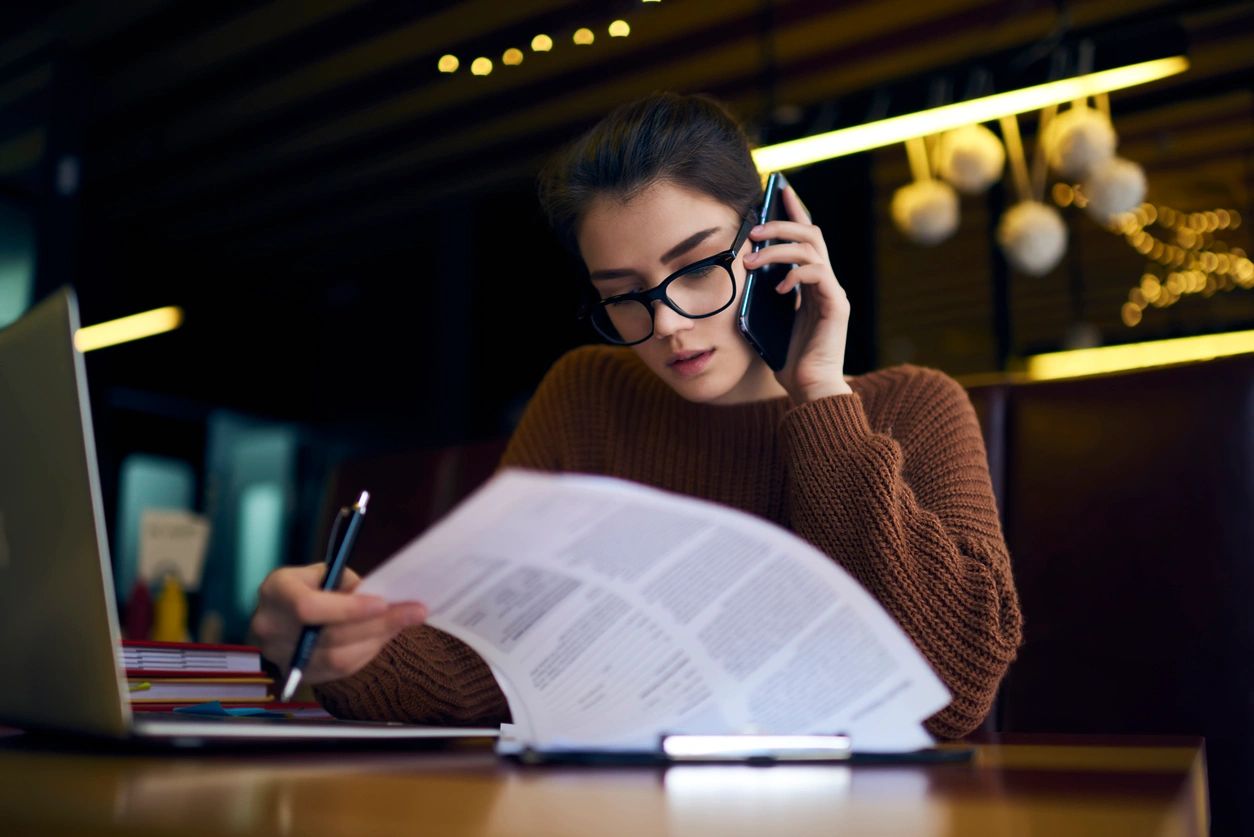 Online Reading: Woman reviewing paperwork while making a phone call.