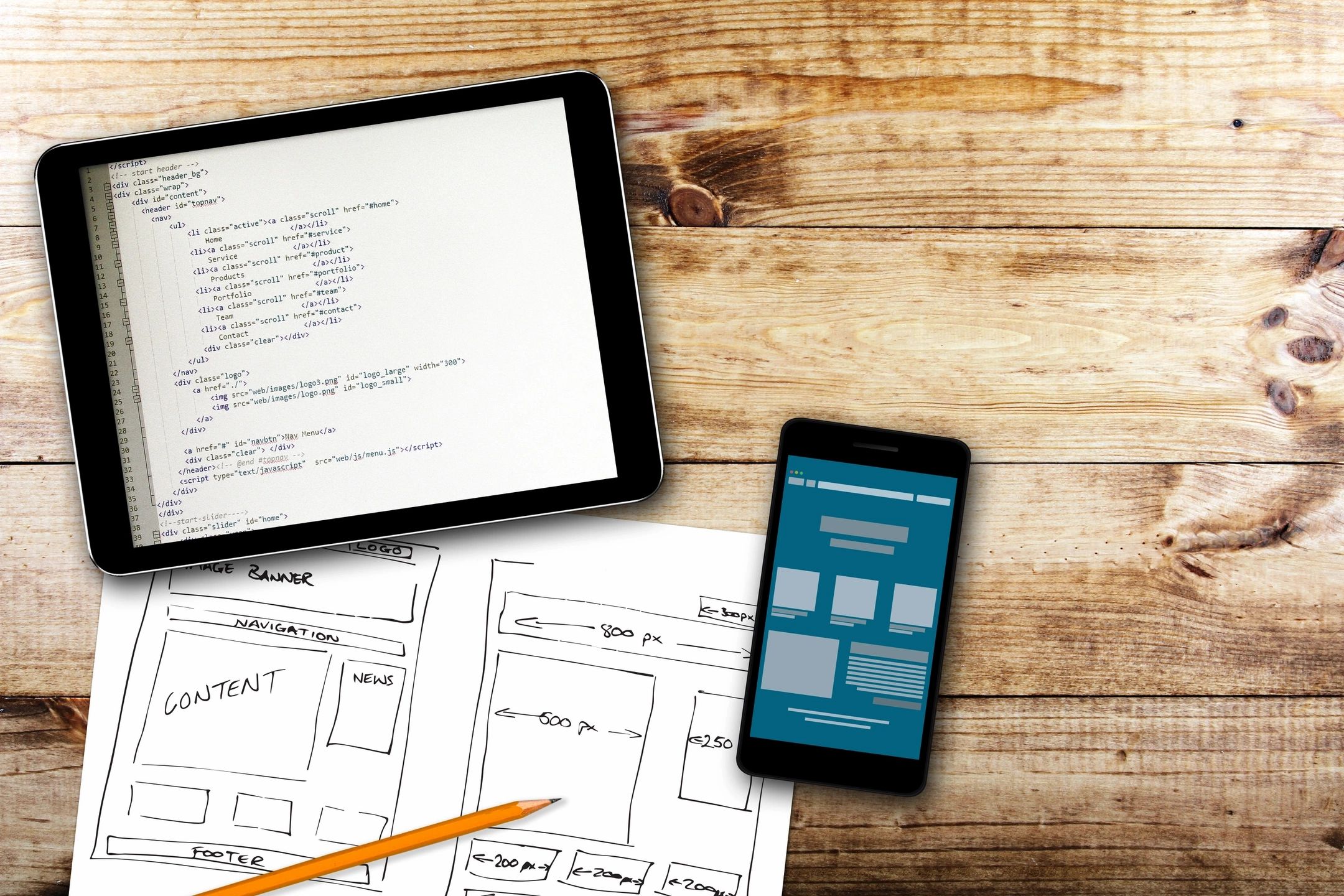 Dispositivos móviles (smartphone, iPad) y folios con bocetos de la estructura de un sitio web.