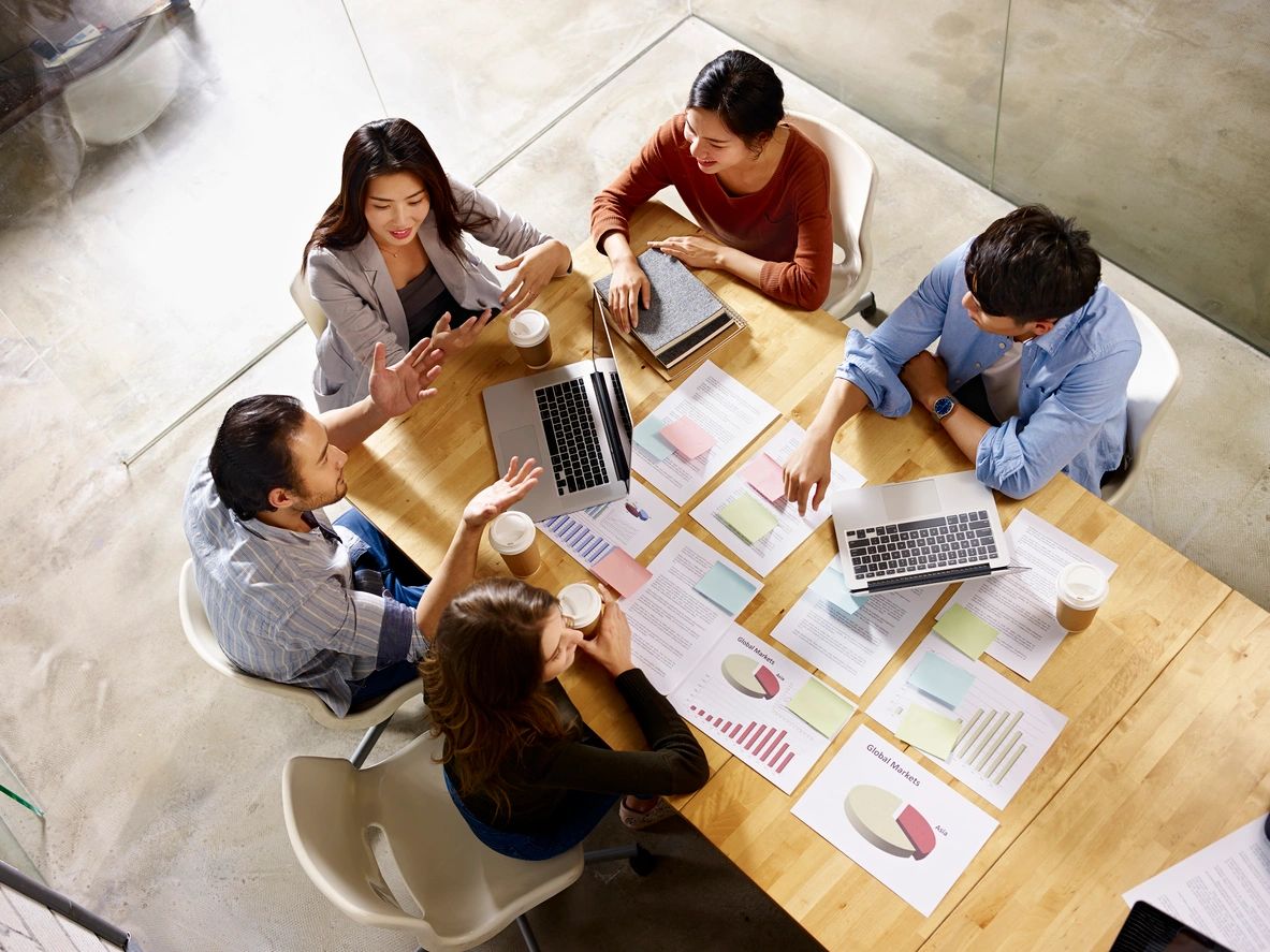 Team gathered around a table with laptops and reports