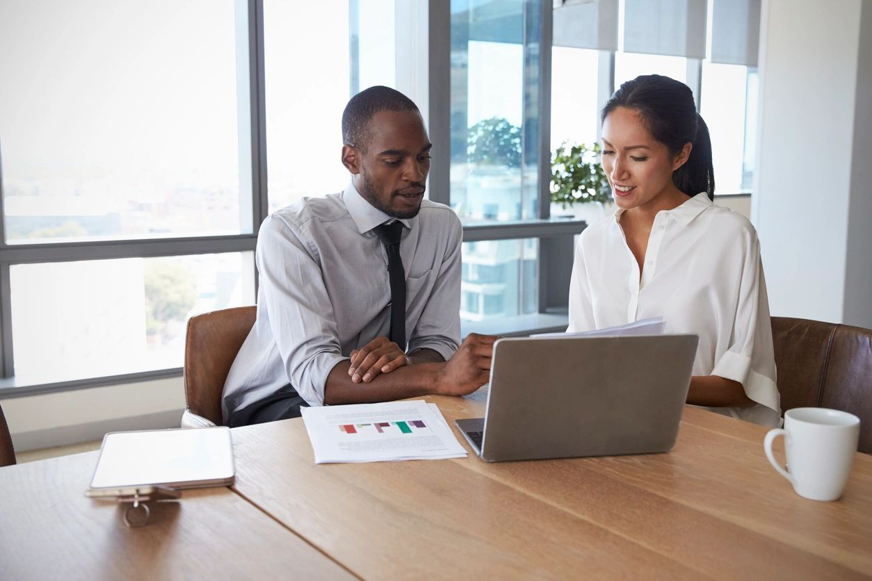 Two analysts reviewing printed graphs while looking at a computer screen. UX Professionals